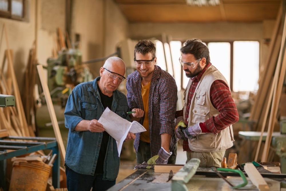 Multigenerational,Group,Of,Carpenters,Working,Together,In,A,Woodworking,Workshop